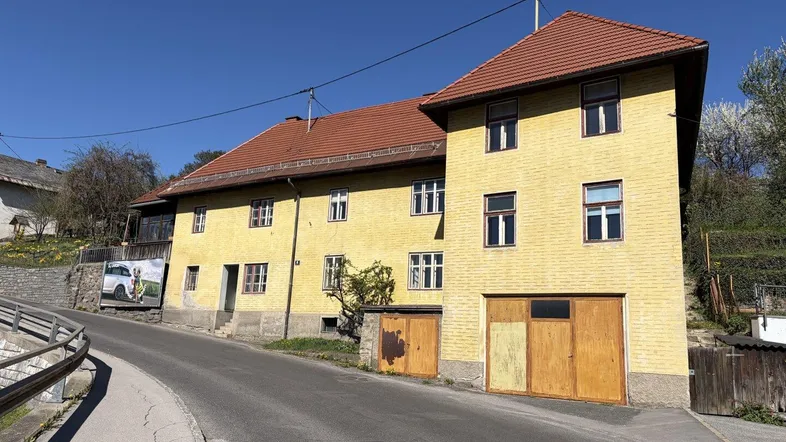 Gelbes Gebäude mit rotem Ziegeldach und einer Garage an einer kurvigen Straße gelegen.