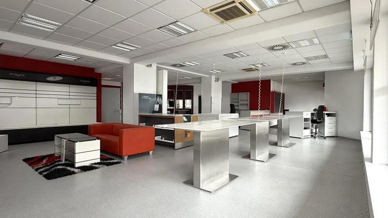 Geräumiger Verkaufsraum mit modernen Präsentationstischen, einer Sitzecke und abgehängter Decke.