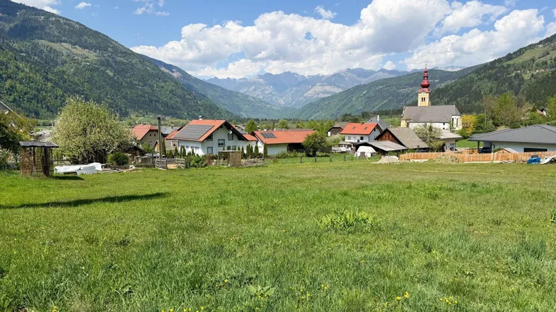 Weitläufige grüne Wiese mit Blick auf die umliegenden Berge und ein Dorf mit Kirche.