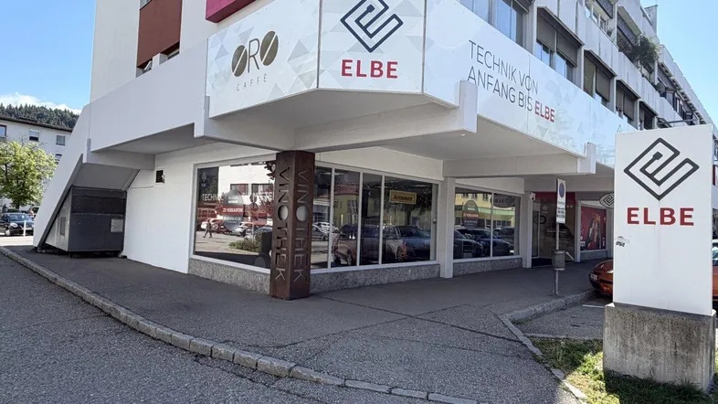 Außenansicht eines modernen Geschäftsgebäudes mit großen Schaufenstern und Firmenlogos an der Ecke.