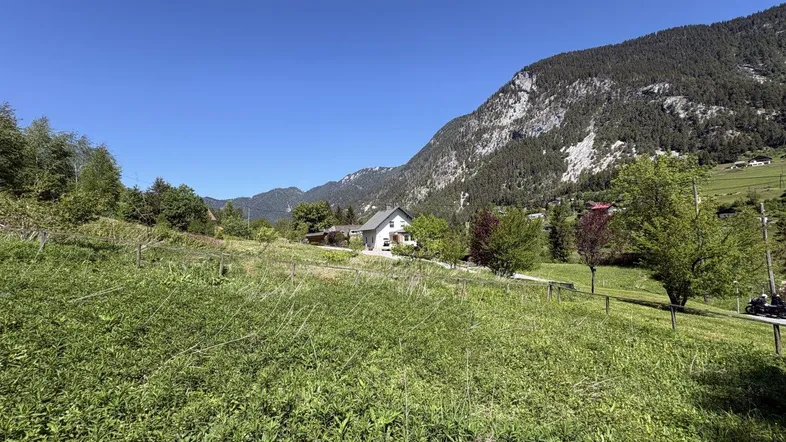 Haus in ländlicher Umgebung mit weitem Blick auf die Berge und grüne Wiesen unter blauem Himmel.