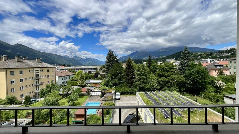 Blick vom Balkon auf die umliegende Berglandschaft, Gebäude und einen Poolbereich.