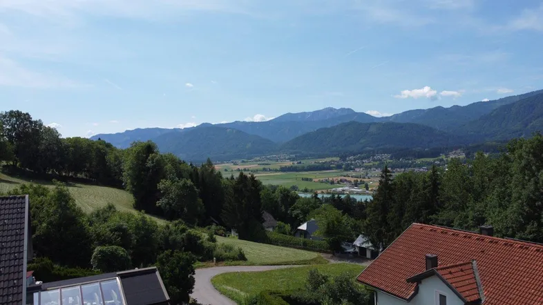Panoramablick über ein grünes Tal mit Bergen, Häusern und einem See in der Ferne.