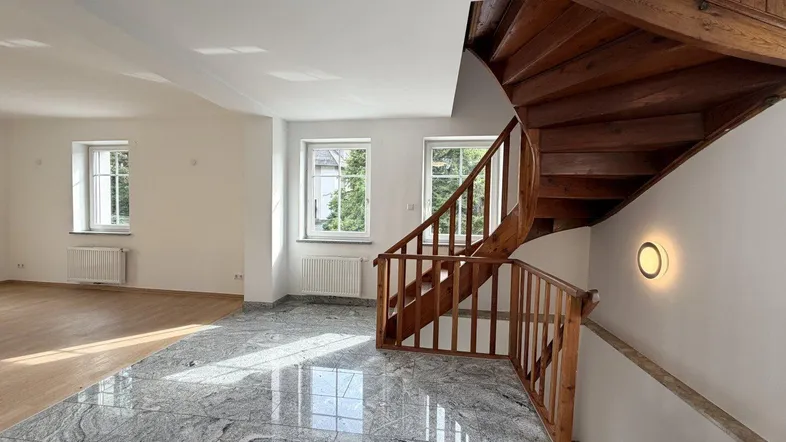 Geräumiger Flur mit eleganter Holzwendeltreppe und glänzendem grauen Fliesenboden, hell durch Fenster.