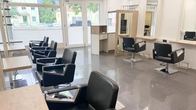 Geräumiger Friseursalon mit mehreren Styling-Stationen, großen Spiegeln und viel Tageslicht durch die Fensterfront.