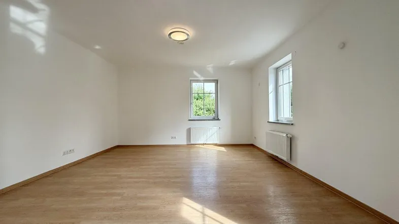 Helles, leeres Zimmer mit Parkettboden und zwei Fenstern, bereit zur individuellen Gestaltung.
