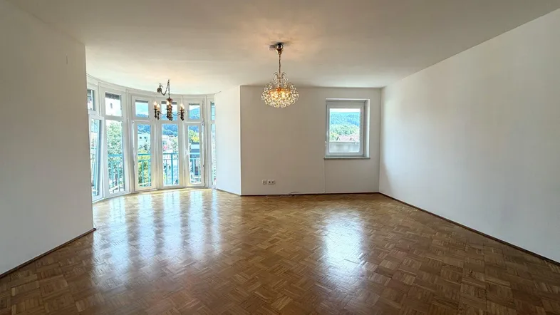 Helles Wohnzimmer mit Fischgrätparkett, großen Fenstern und Bergblick, ausgestattet mit einem Kronleuchter.