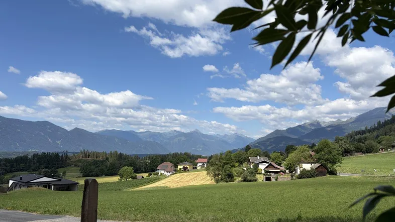 Malerischer Blick auf eine ländliche Landschaft mit Bergen, grünen Feldern und vereinzelten Häusern unter blauem Himmel.