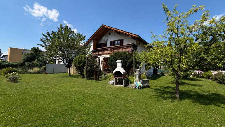 Gepflegter Garten mit Rasenfläche, Bäumen und einem gemauerten Grillplatz vor dem Haus.