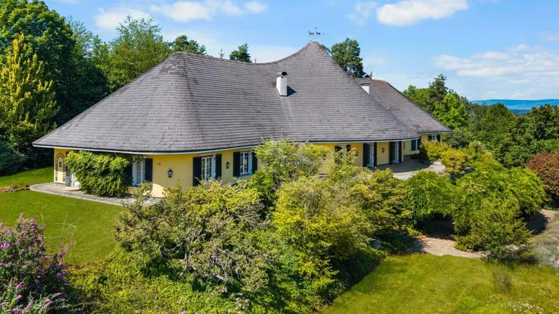 Großzügiges Anwesen mit weitläufigem Garten und traditioneller Architektur unter blauem Himmel.