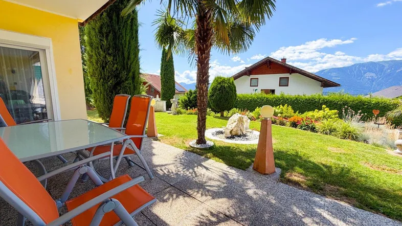 Sonnige Terrasse mit Gartenmöbeln, Palmen und Blick auf die Berge und den Garten.