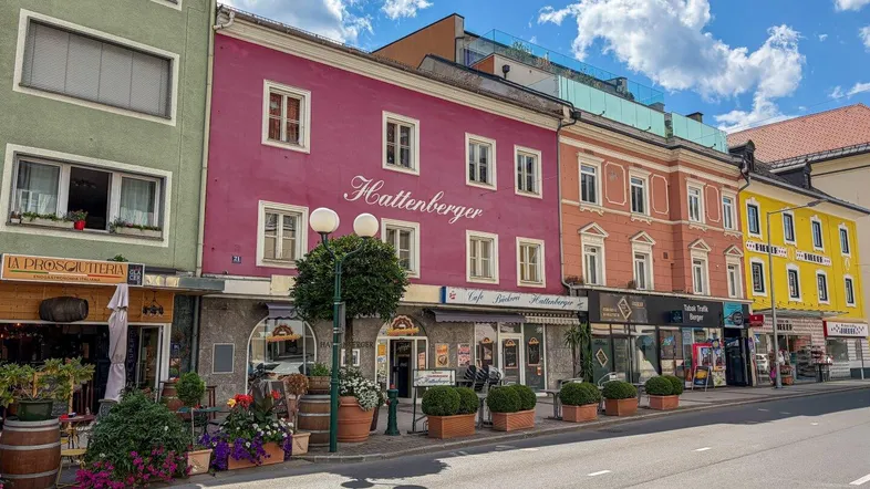 Bunte Gebäude entlang einer belebten Straße mit Geschäften im Erdgeschoss unter blauem Himmel.