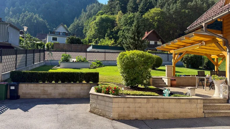 Gepflegter Gartenbereich mit Rasenfläche, Hochbeeten und einer überdachten Terrasse mit Bergblick.