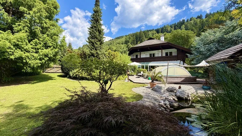 Großer, gepflegter Garten mit Teich, Rasenflächen und üppiger Vegetation vor dem Haus.
