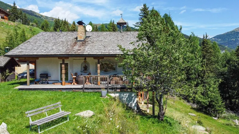 Traditionelles Chalet in alpiner Umgebung mit Holzdach, kleiner Veranda und weitem Bergblick.