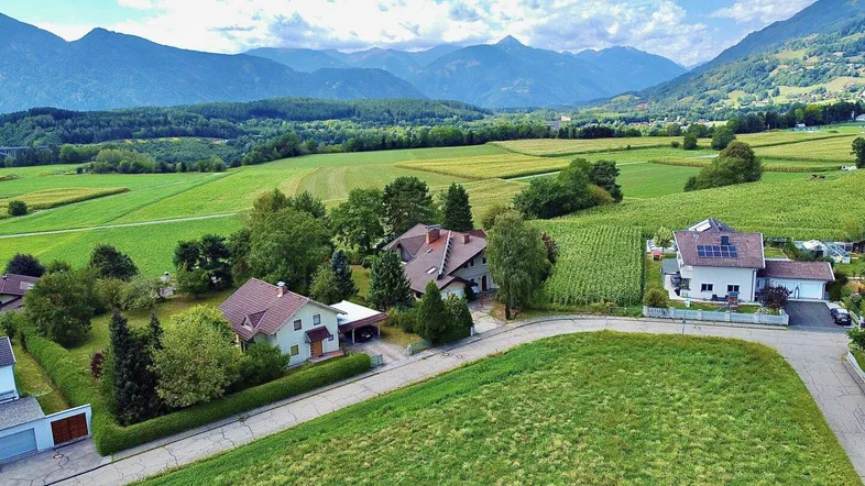 Luftaufnahme von Häusern in einer grünen Talandschaft mit majestätischen Bergen im Hintergrund.