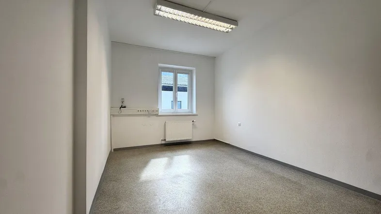 Heller, leerer Raum mit Fenster, Heizkörper und einem kleinen Waschbeckenbereich, ideal als Büro oder Arbeitszimmer.