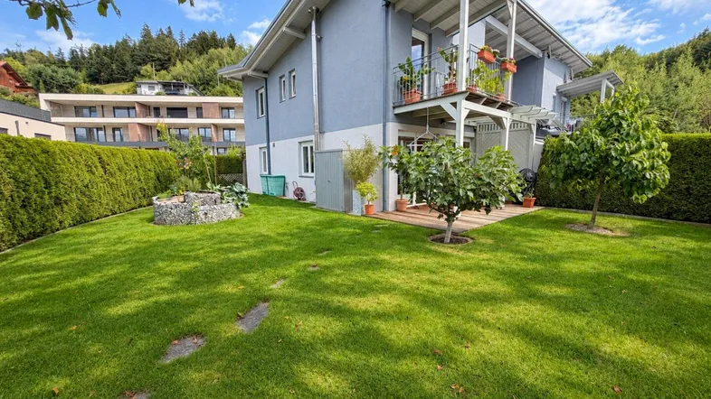 Gepflegter Gartenbereich mit Rasenfläche, Hecke und Blick auf das moderne Haus.
