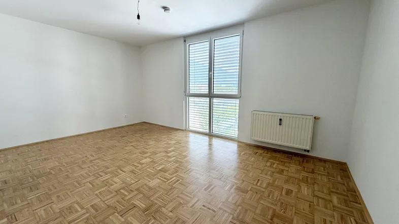 Helles Zimmer mit Parkettboden und großem Fenster, das viel Tageslicht hereinlässt.
