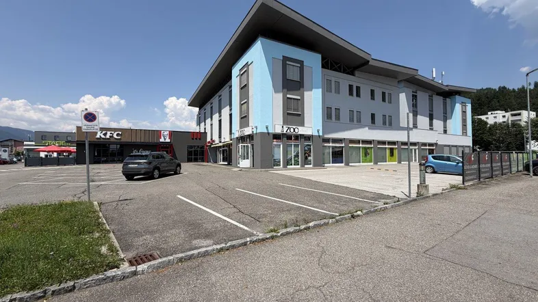 Modernes Gebäude mit blauen Akzenten und großem Parkplatz, umgeben von Gewerbeflächen.