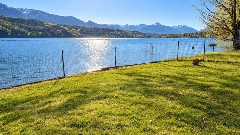 Sonniger Gartenbereich direkt am See mit weitem Blick auf die beeindruckende Bergkulisse.