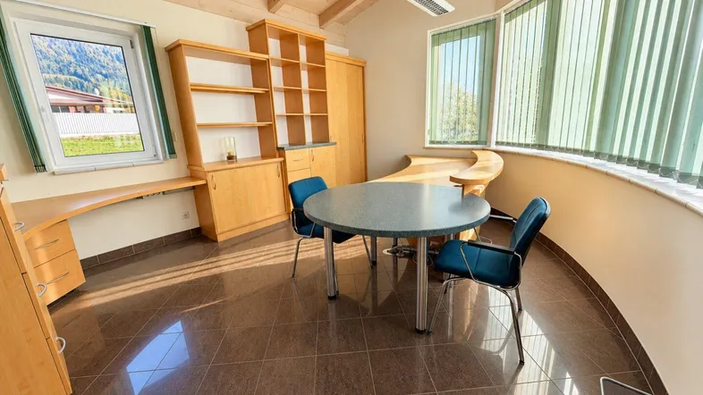 Helles Büro mit Holzbalkendecke, braunen Fliesen und großen Fenstern mit Bergblick.