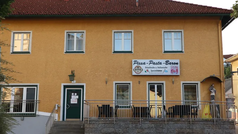 Gelbes Gebäude mit rotem Ziegeldach und einem Restaurant im Erdgeschoss mit Außenterrasse.