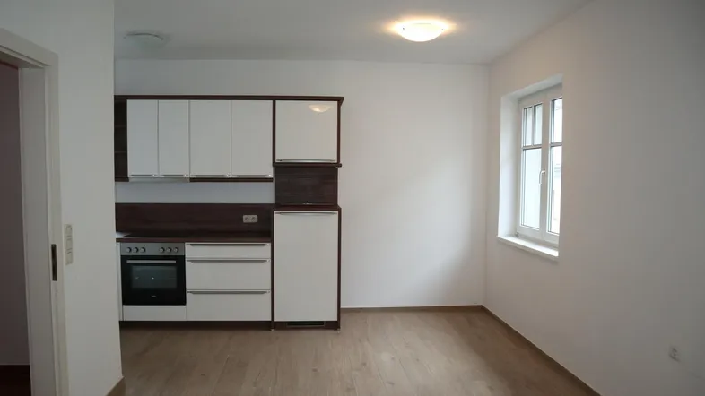 Kompakte Einbauküche mit weißen Schränken und Holzdekor, integriert in einen hellen Raum mit Fenster.