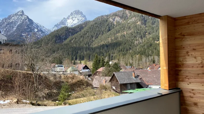 Blick von einem überdachten Balkon auf eine malerische Berglandschaft und ein Dorf.