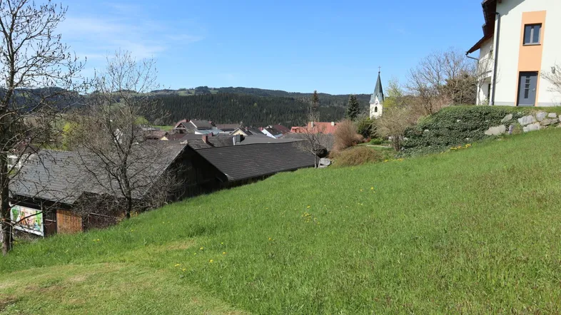 Grüne Hügellandschaft mit Blick auf ein Dorf und eine Kirche im Hintergrund unter blauem Himmel.