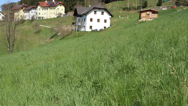 Blick auf ein weißes Haus mit braunem Dach und umliegende grüne Hügellandschaft unter blauem Himmel.