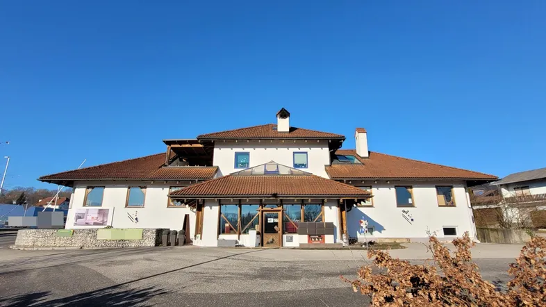 Das Gebäude präsentiert sich mit einer hellen Fassade und einem markanten Ziegeldach unter blauem Himmel.