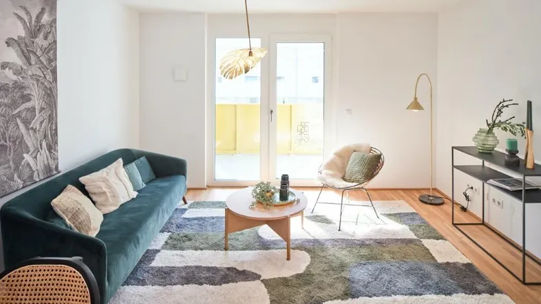 Helles Wohnzimmer mit modernem Teppich, bequemer Couch und Zugang zum Balkon.