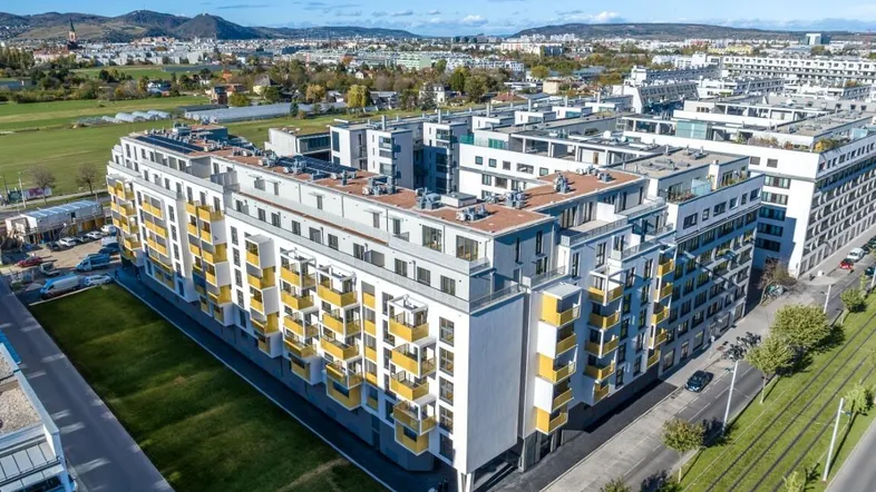 Luftaufnahme eines modernen Wohnkomplexes mit vielen Balkonen und begrünten Flächen in städtischer Umgebung.