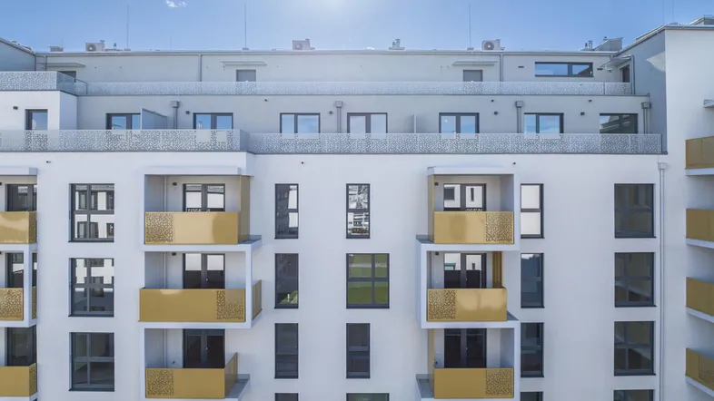 Moderne Wohnhausfassade mit zahlreichen Balkonen und dekorativen goldenen Geländern unter blauem Himmel.