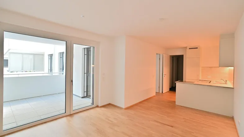 Heller offener Wohn-Essbereich mit Parkettboden und Zugang zu einem geräumigen Balkon.