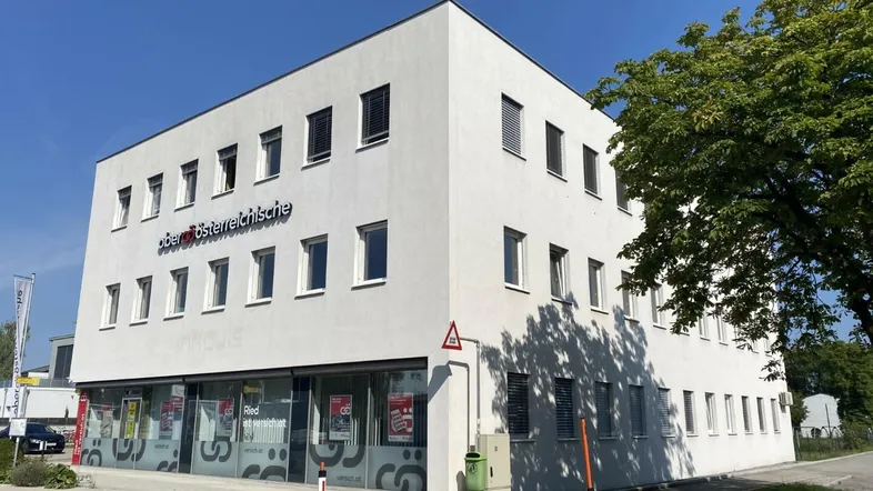 Modernes, weißes Geschäftsgebäude mit großen Fenstern und Jalousien unter klarem blauem Himmel.