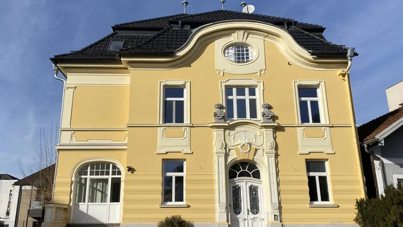 Historisches Gebäude mit gelber Fassade, reich verzierten Details und Mansarddach unter blauem Himmel.