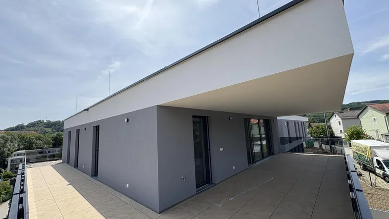 Große, geflieste Terrasse im Obergeschoss eines modernen Gebäudes mit weitem Blick.