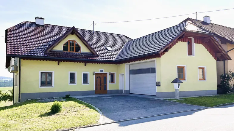 Traditionelles Einfamilienhaus mit gelber Fassade, Satteldach und integrierter Garage.