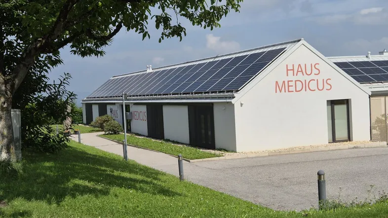 Modernes Gebäude mit Photovoltaikanlage auf dem Dach und Beschriftung "HAUS MEDICUS" in ländlicher Umgebung.