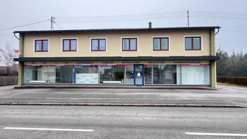 Gebäudeansicht eines Gewerbeobjekts mit großen Schaufenstern und Parkplätzen davor.