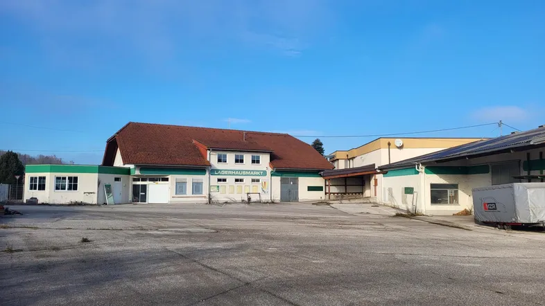 Außenansicht eines Lagerhausmarktes mit großem asphaltierten Parkplatz unter blauem Himmel.