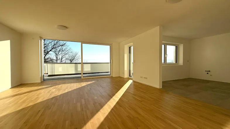 Helles und geräumiges Wohnzimmer mit Parkettboden, großen Fenstern und Zugang zum Balkon.