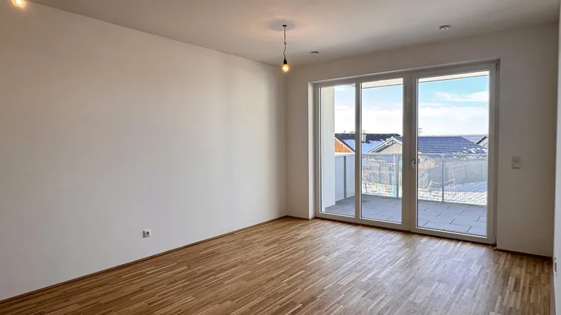 Helles, leeres Zimmer mit Parkettboden und Zugang zu einem großen Balkon.
