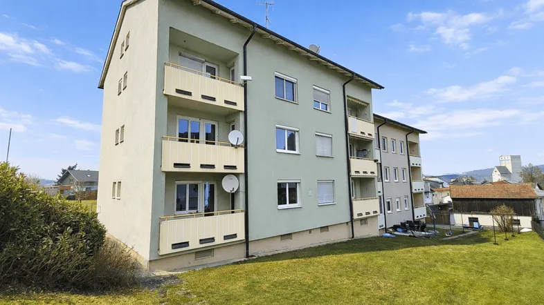 Mehrfamilienhaus mit hellgrüner Fassade, Balkonen und großem Rasenbereich unter blauem Himmel.