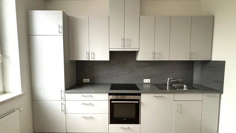 Moderne Einbauküche in Hellgrau mit integrierten Geräten, dunkler Arbeitsplatte und Fenster.