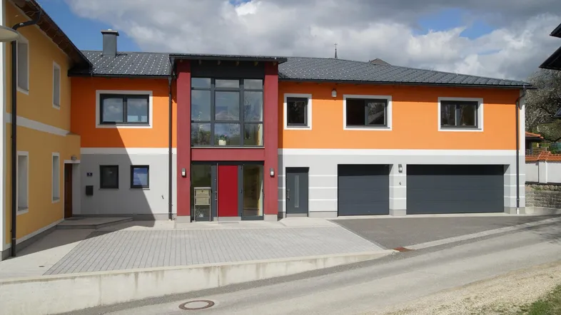 Modernes Gebäude mit orangefarbener Fassade, großem Glasportal und zwei Garagen.