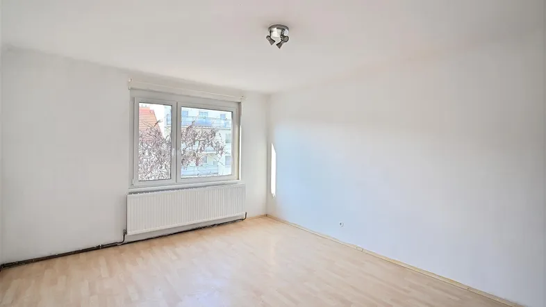 Helles, leeres Zimmer mit Parkettboden und großem Fenster, bereit zur individuellen Gestaltung.