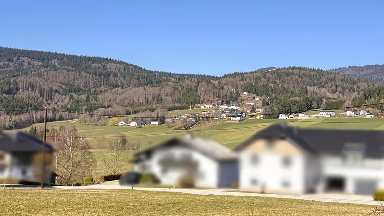 Weitläufige Landschaft mit grünen Hügeln und verstreuten Häusern unter blauem Himmel.